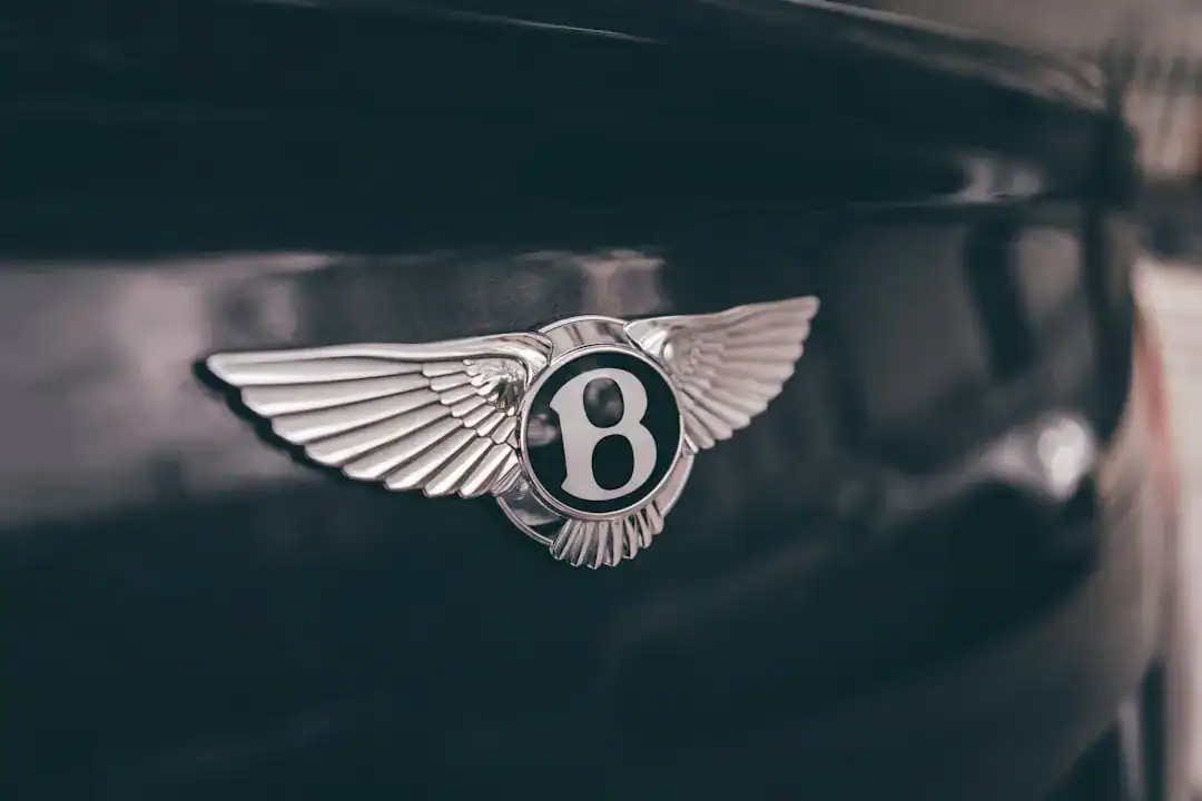 Illustration of Close-up macro photography of a metallic silver winged car emblem on a glossy black luxury vehicle.
