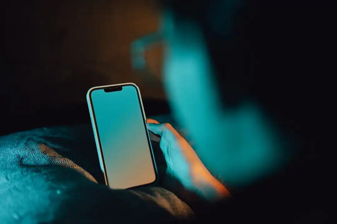 Hand holding a smartphone in a dimly lit room with teal glow