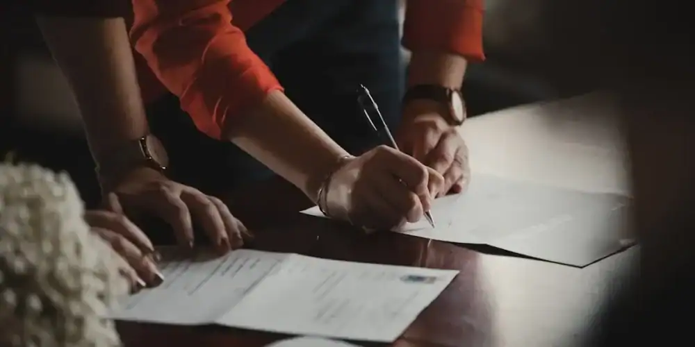 Close-up of hands signing documents at a wooden table