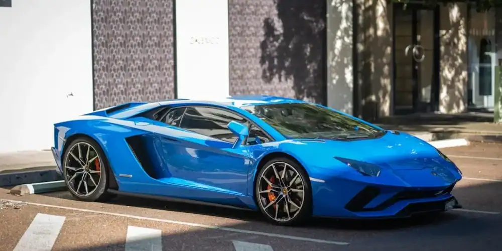Blue Lamborghini Aventador parked on a sunny city street beside a white storefront