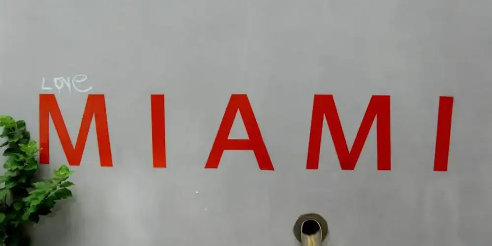Gray wall with red MIAMI letters, a white 'LOVE' graffiti, a circular pipe, and greenery