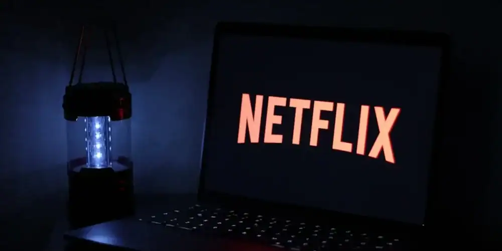 Laptop displaying Netflix logo in a dark room beside a glowing blue lantern