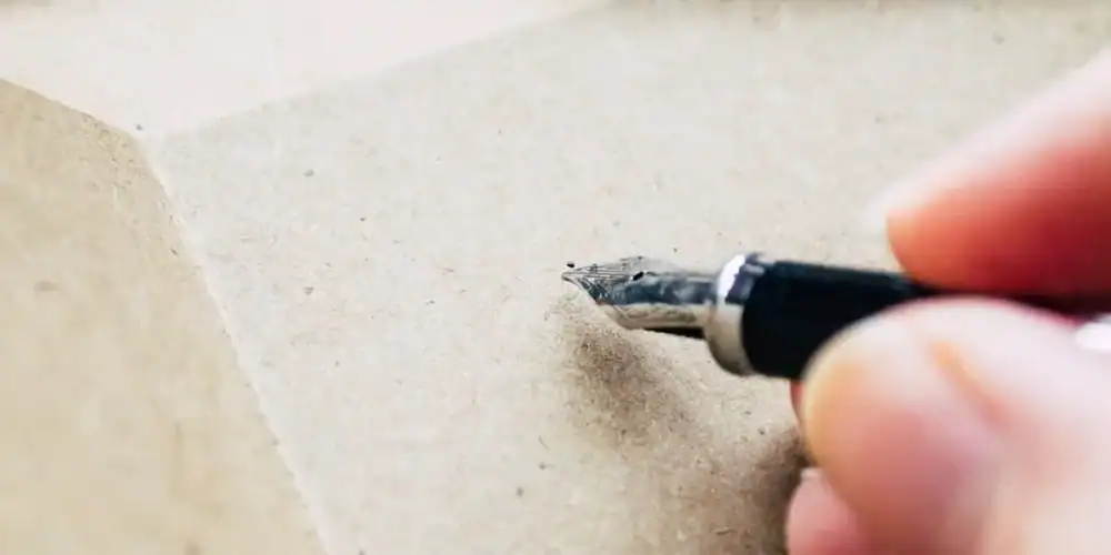 Close-up of a hand using a craft knife to cut brown cardboard