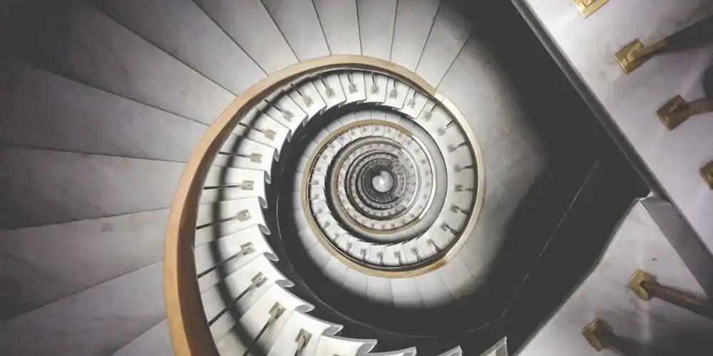Overhead view of a spiral marble staircase with white steps and gold railings