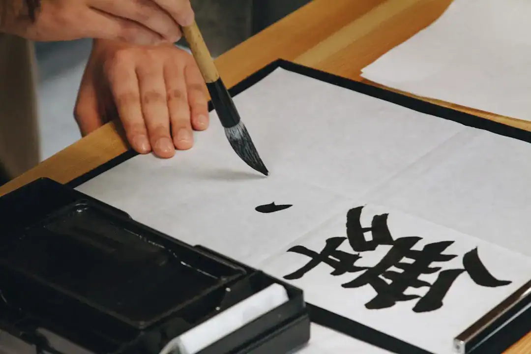 Hand holding a brush writing Chinese calligraphy on paper