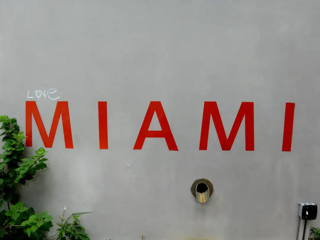 Gray wall with red MIAMI letters, a white 'LOVE' graffiti, a circular pipe, and greenery
