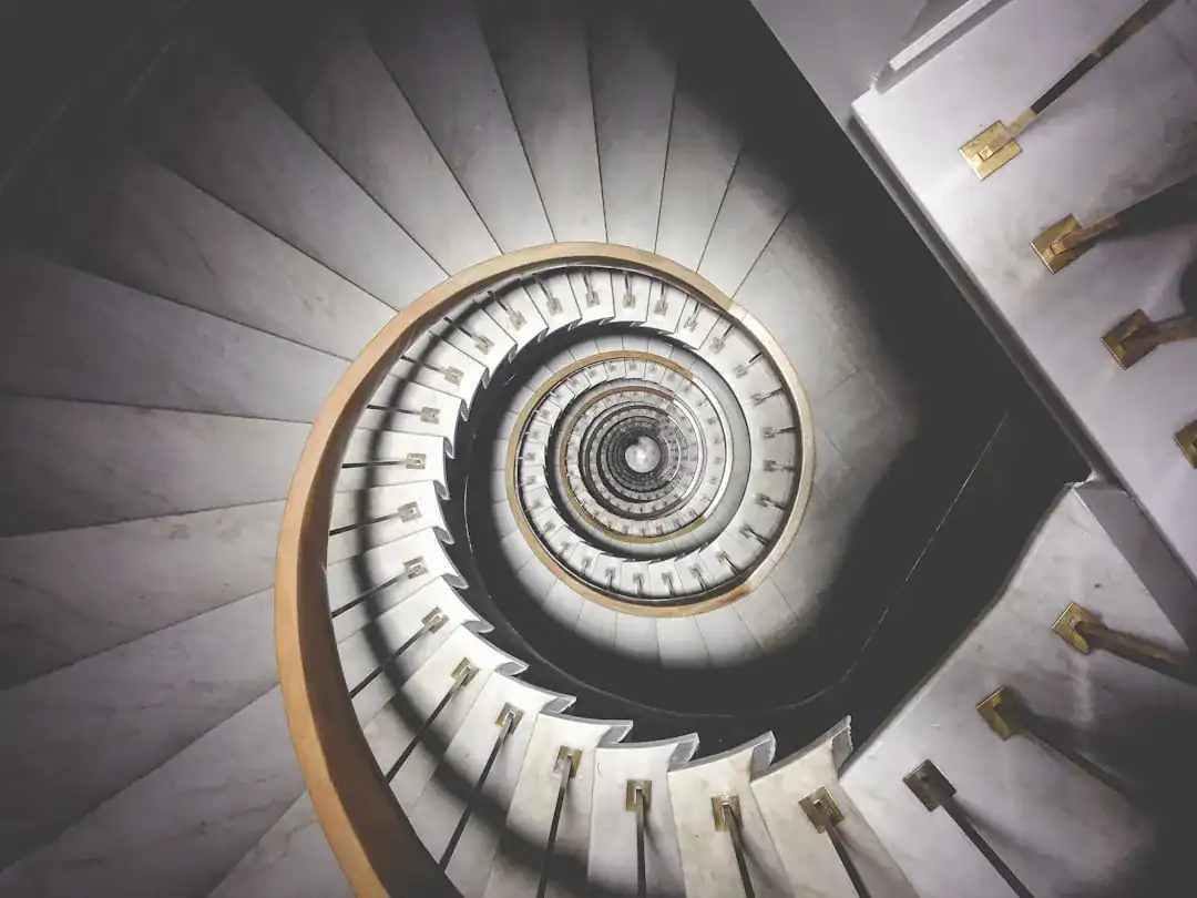 Overhead view of a spiral marble staircase with white steps and gold railings