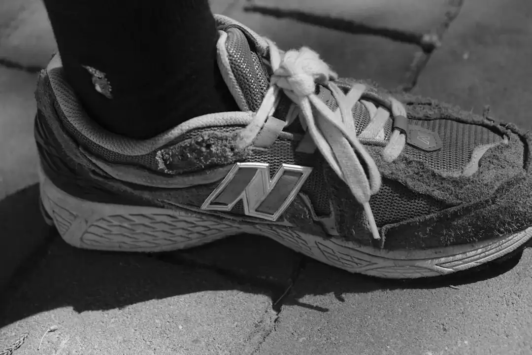 Close-up of a worn New Balance sneaker with untied laces on cracked pavement