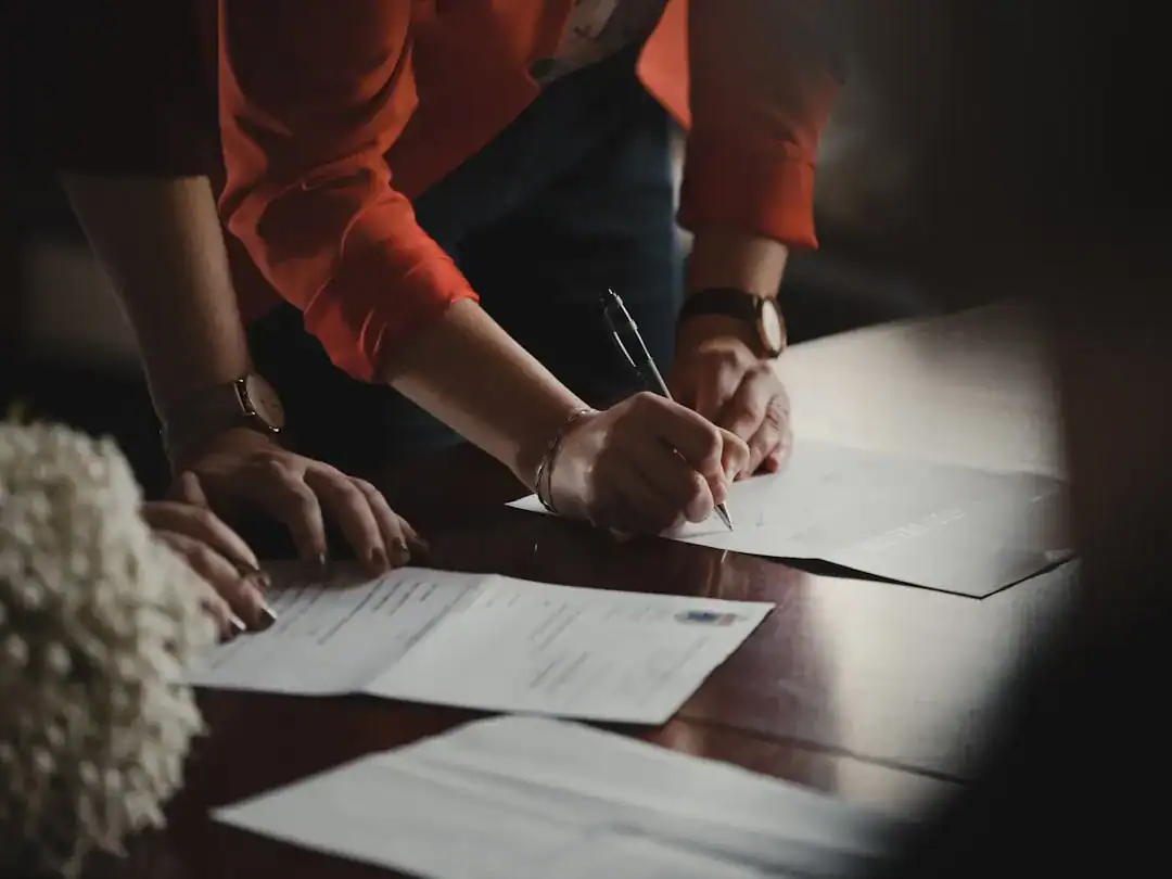 Close-up of hands signing documents at a wooden table
