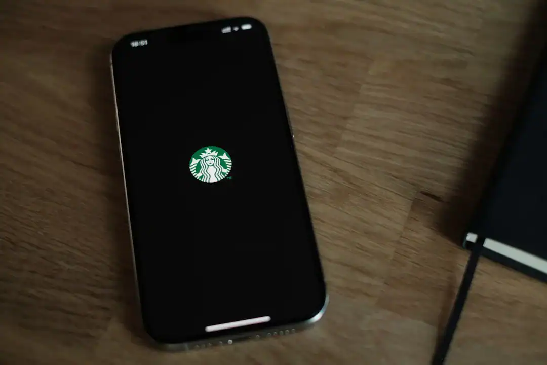 Smartphone on wooden desk showing Starbucks logo on screen with a notebook beside it