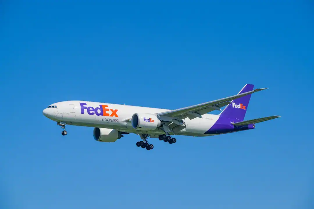 FedEx Express cargo plane in flight with landing gear down against blue sky