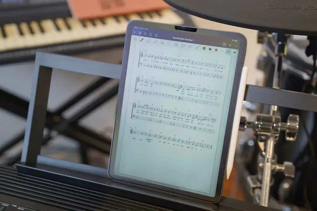 Tablet on a music stand displaying sheet music with keyboard and drums nearby