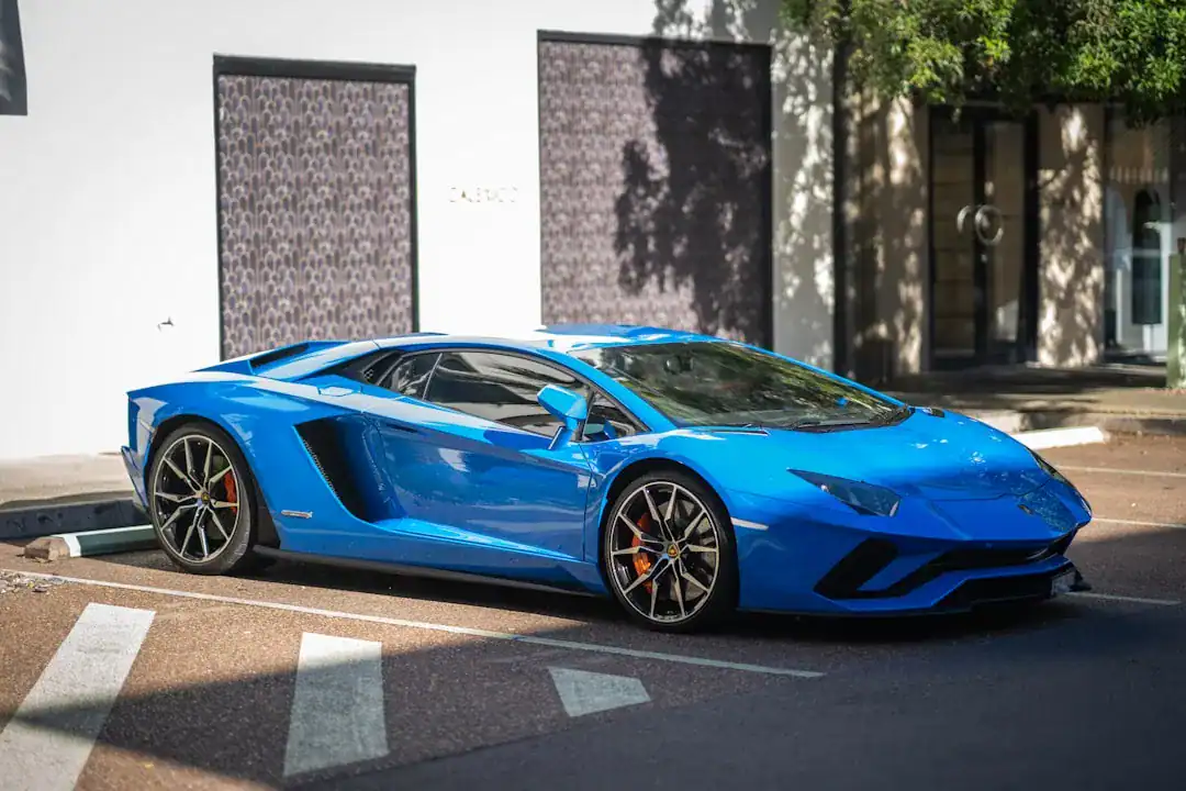 Blue Lamborghini Aventador parked on a sunny city street beside a white storefront