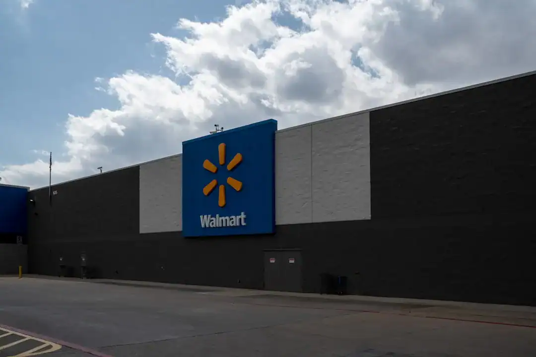 Walmart storefront exterior with blue sign and yellow logo on a dark wall, empty parking lot under a cloudy sky