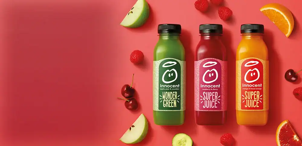 Three Innocent juice bottles in green, pink, and orange with fruit slices on a pink background.