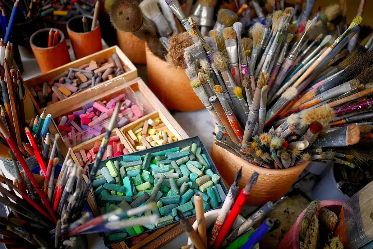 Studio with paintbrushes in cups and boxes of soft pastels and pencils