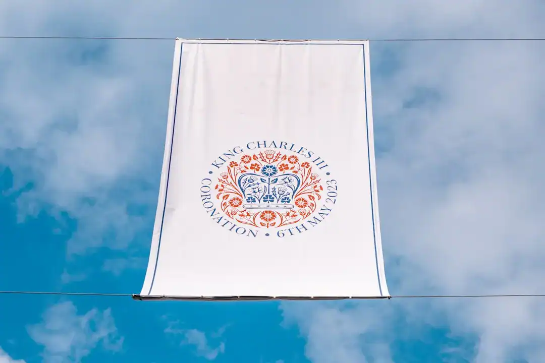 White coronation banner with floral crest and text for King Charles III, hanging in the blue sky