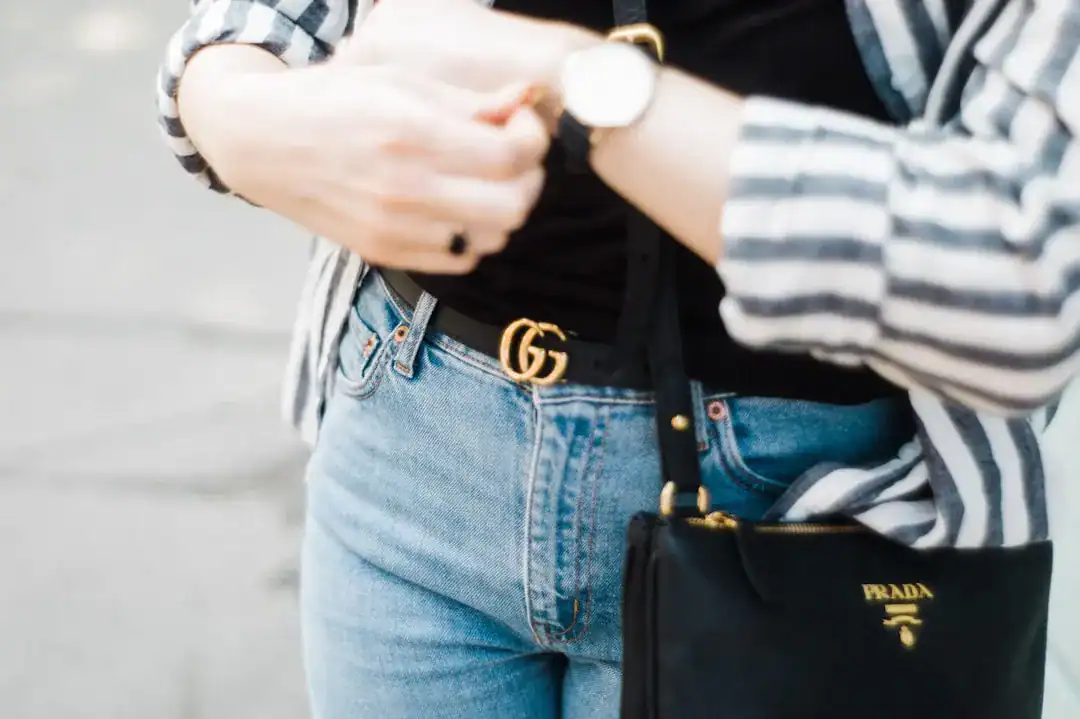 Close-up of a casual outfit featuring denim jeans, striped shirt, Gucci belt and Prada handbag