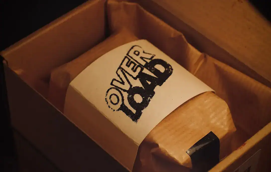 Brown paper-wrapped item in a box with an OVERLOAD label