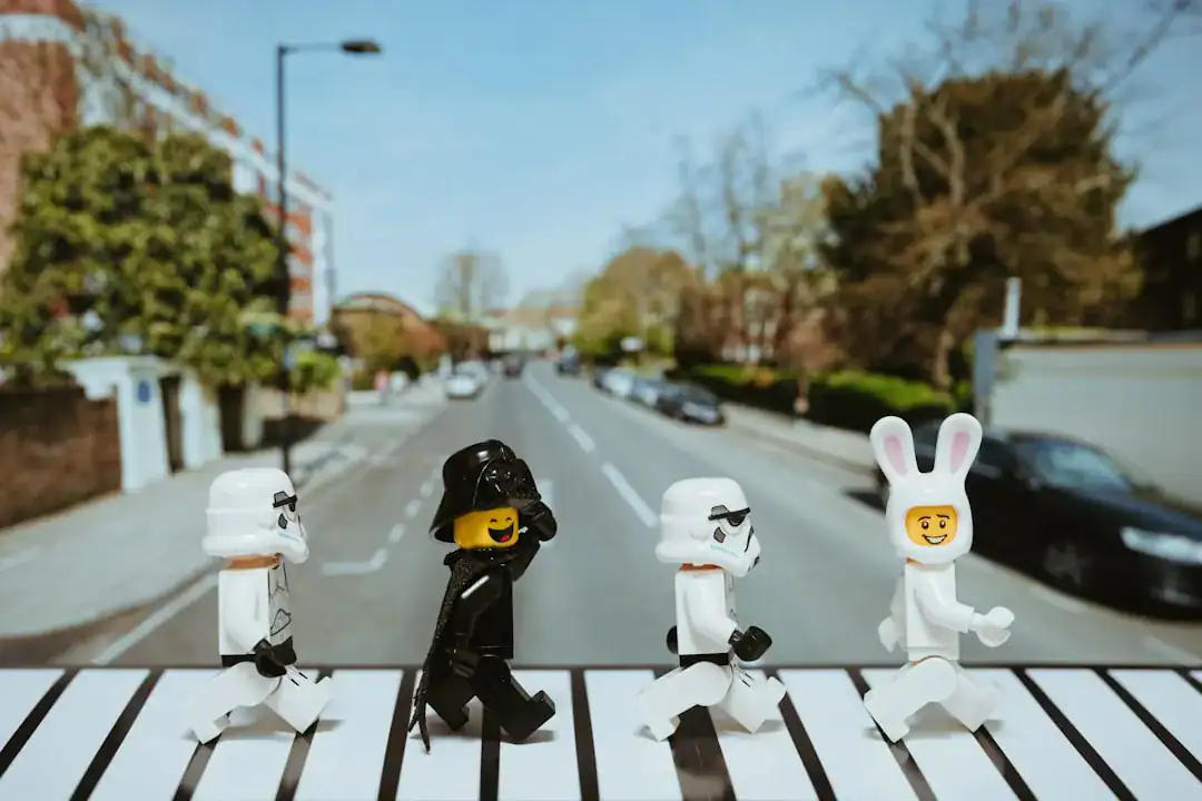 LEGO minifigures crossing a zebra crosswalk on a suburban street with houses in the background