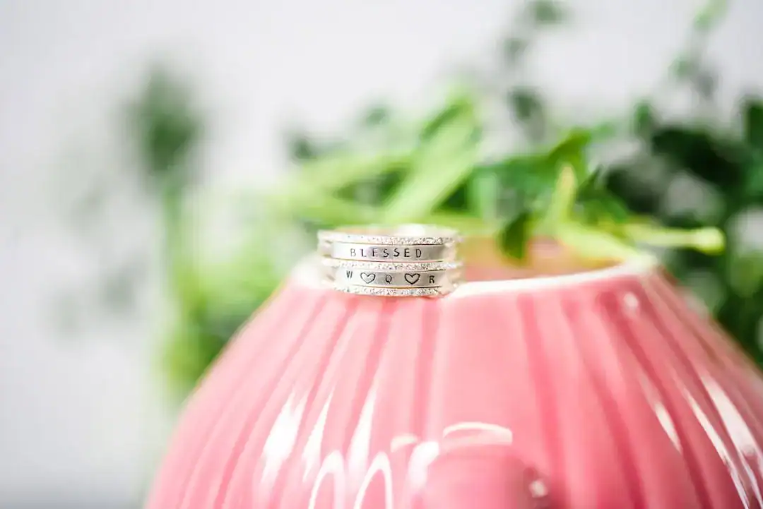 Two silver engraved rings stacked on a pink ribbed lantern with a blurred green plant backdrop