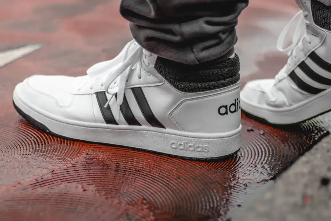 White Adidas sneakers with black stripes on a wet red surface