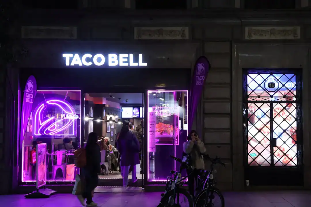 Taco Bell storefront at night with purple neon lighting and people outside