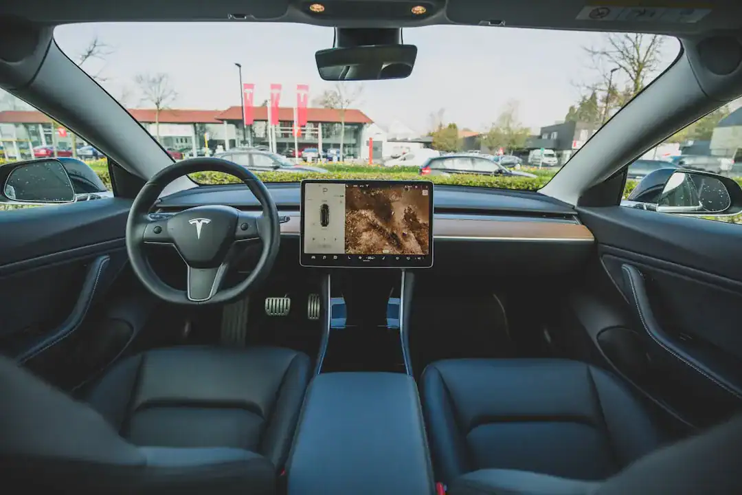 Tesla interior with large central touchscreen and minimalist dashboard as seen from the driver's seat.