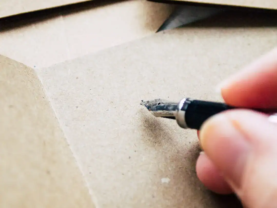 Close-up of a hand using a craft knife to cut brown cardboard