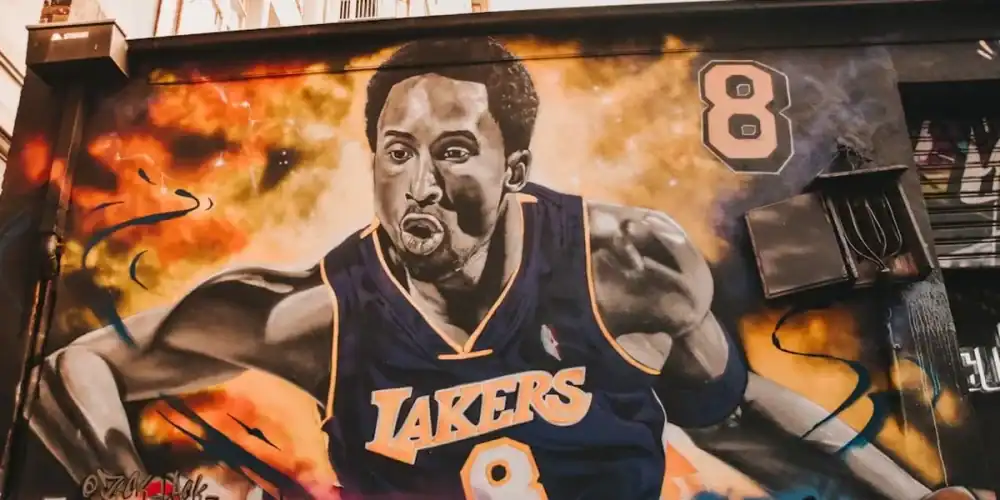 Vibrant street mural of a muscular basketball player in a Lakers jersey #8 against a fiery background