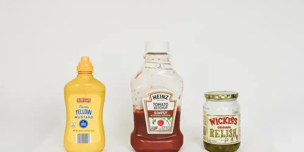 Mustard bottle, ketchup bottle, and relish jar on a white surface