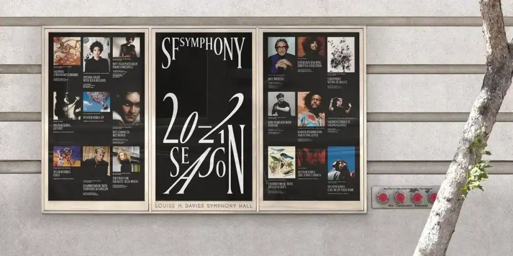 Three framed posters advertising a symphony season mounted on a light concrete wall, with a tree trunk nearby.