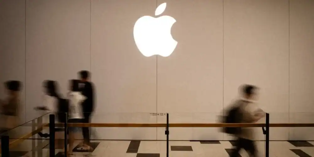 Illuminated Apple logo on wall as pedestrians move past