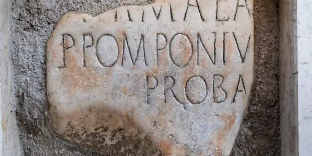 Weathered limestone slab with carved Latin inscription in a rough cement niche