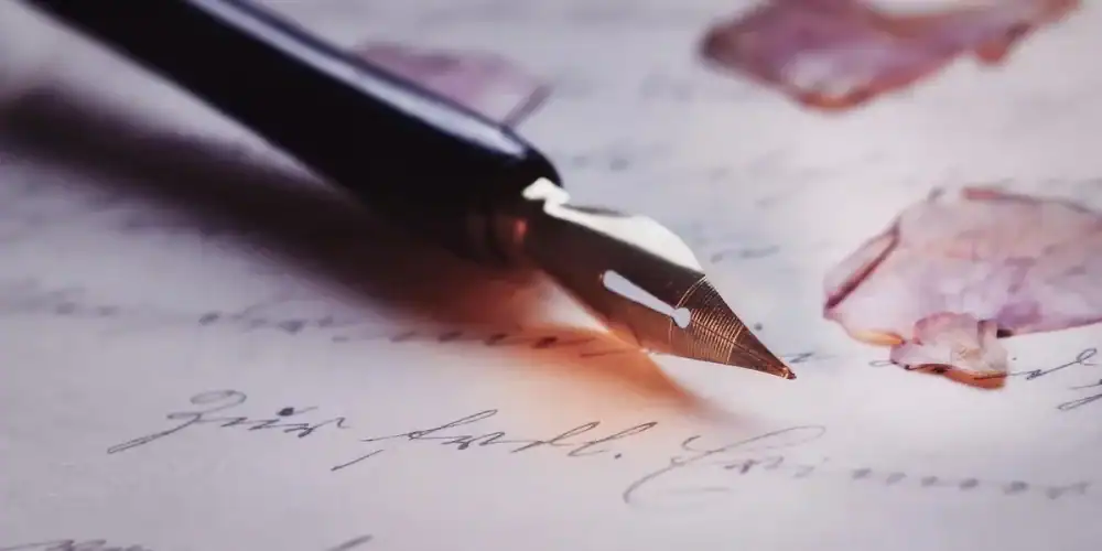 Close-up of a fountain pen nib on cursive handwriting with pink blotches