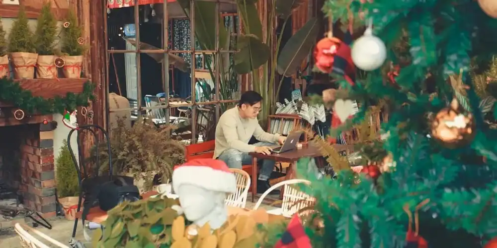 Cozy cafe interior with Christmas tree, greenery, and a laptop user.