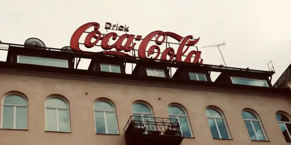Coca-Cola sign on a beige building with arched windows and a small balcony