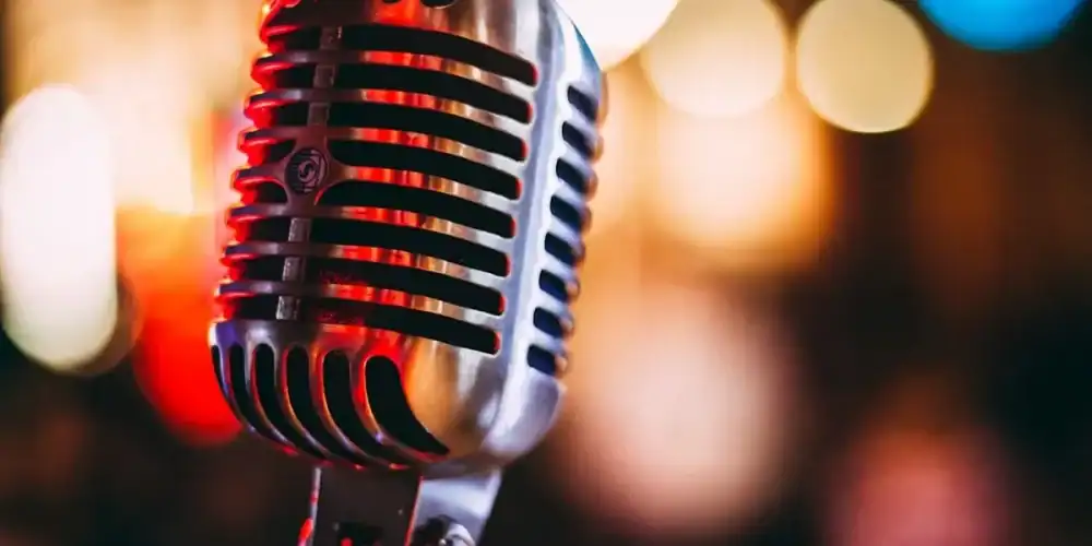 Close-up of a vintage microphone on a stand with colorful stage lights in the background.