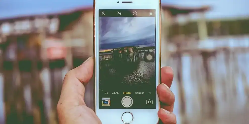 Hand holding iPhone photographing a wooden pier by the water