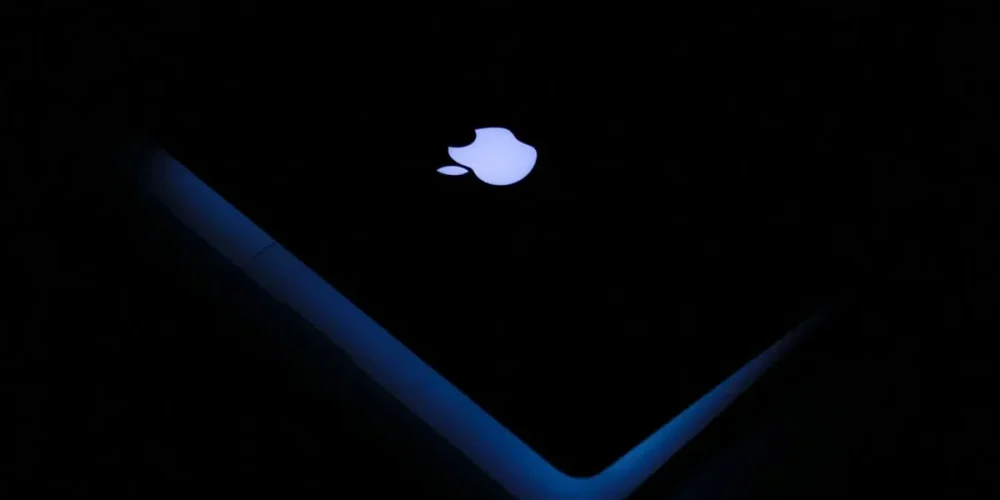 Glowing Apple logo on a dark laptop lid with blue edge lighting