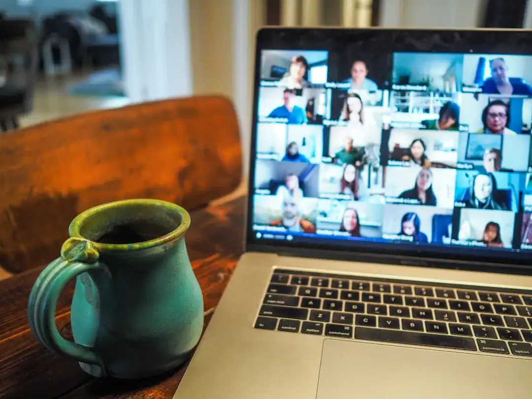 Laptop showing video conference grid and teal mug on a wooden desk