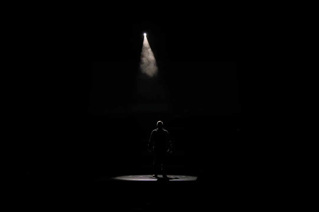 Silhouette of a lone performer under a spotlight on a dark stage.