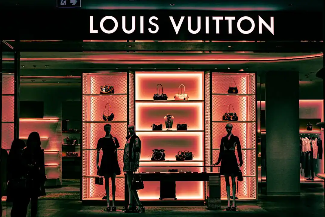 Louis Vuitton storefront with illuminated handbag displays and mannequins, silhouettes of shoppers in front