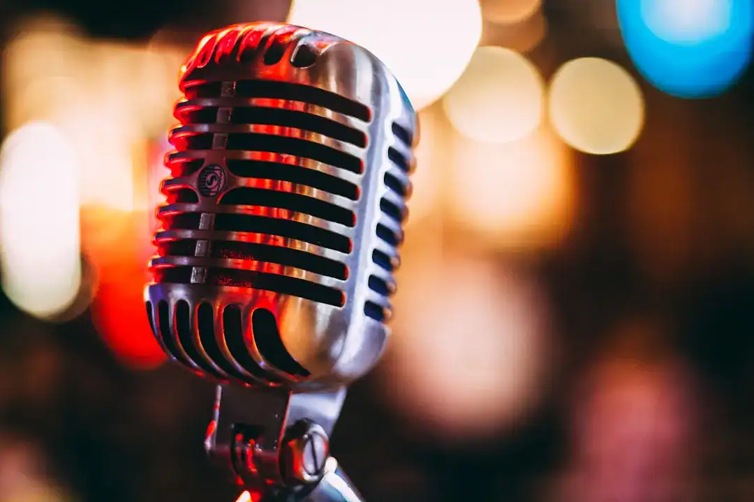 Close-up of a vintage microphone on a stand with colorful stage lights in the background.