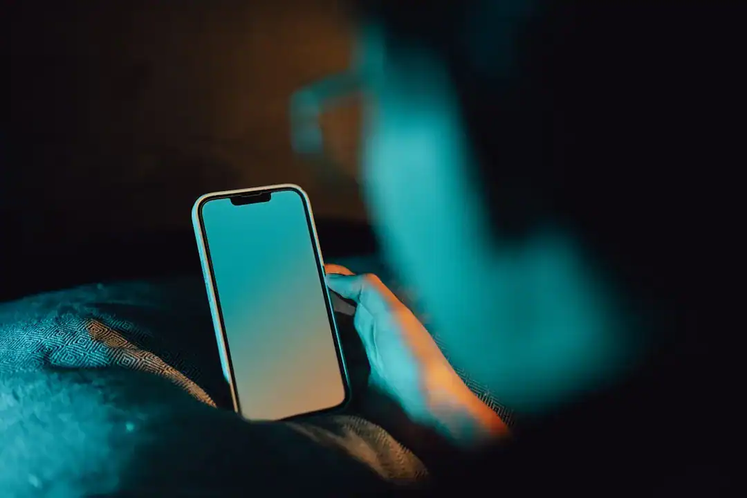 Dim Light, Clear Focus: Phone in Hand Close-up of a hand holding a smartphone in blue-lit darkness
