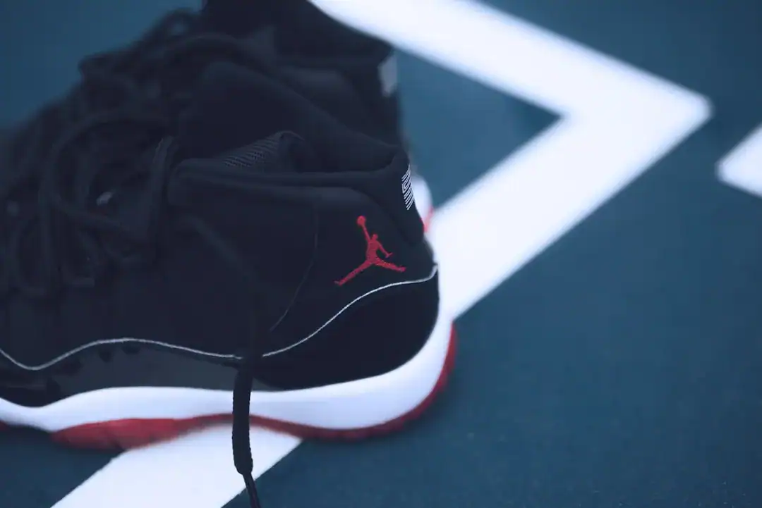Black Jordan sneaker with red Jumpman logo on blue court.