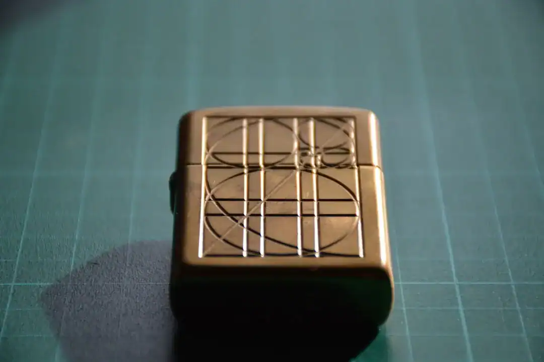 Gold brass lighter with geometric grid engraving on a green cutting mat