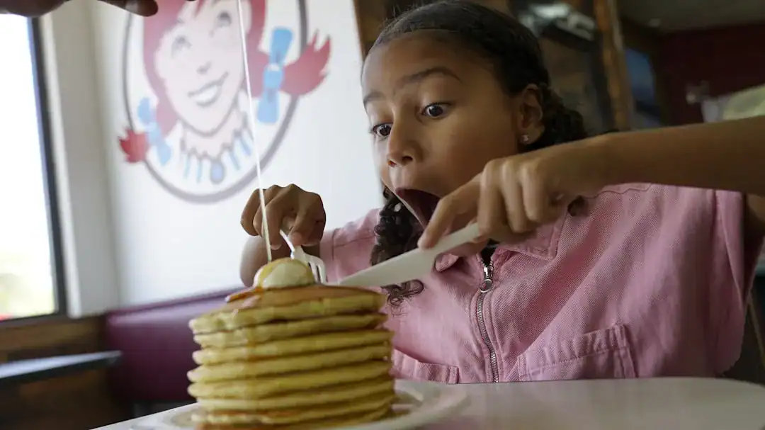Tall stack of golden pancakes on a plate with syrup being poured in a cozy diner