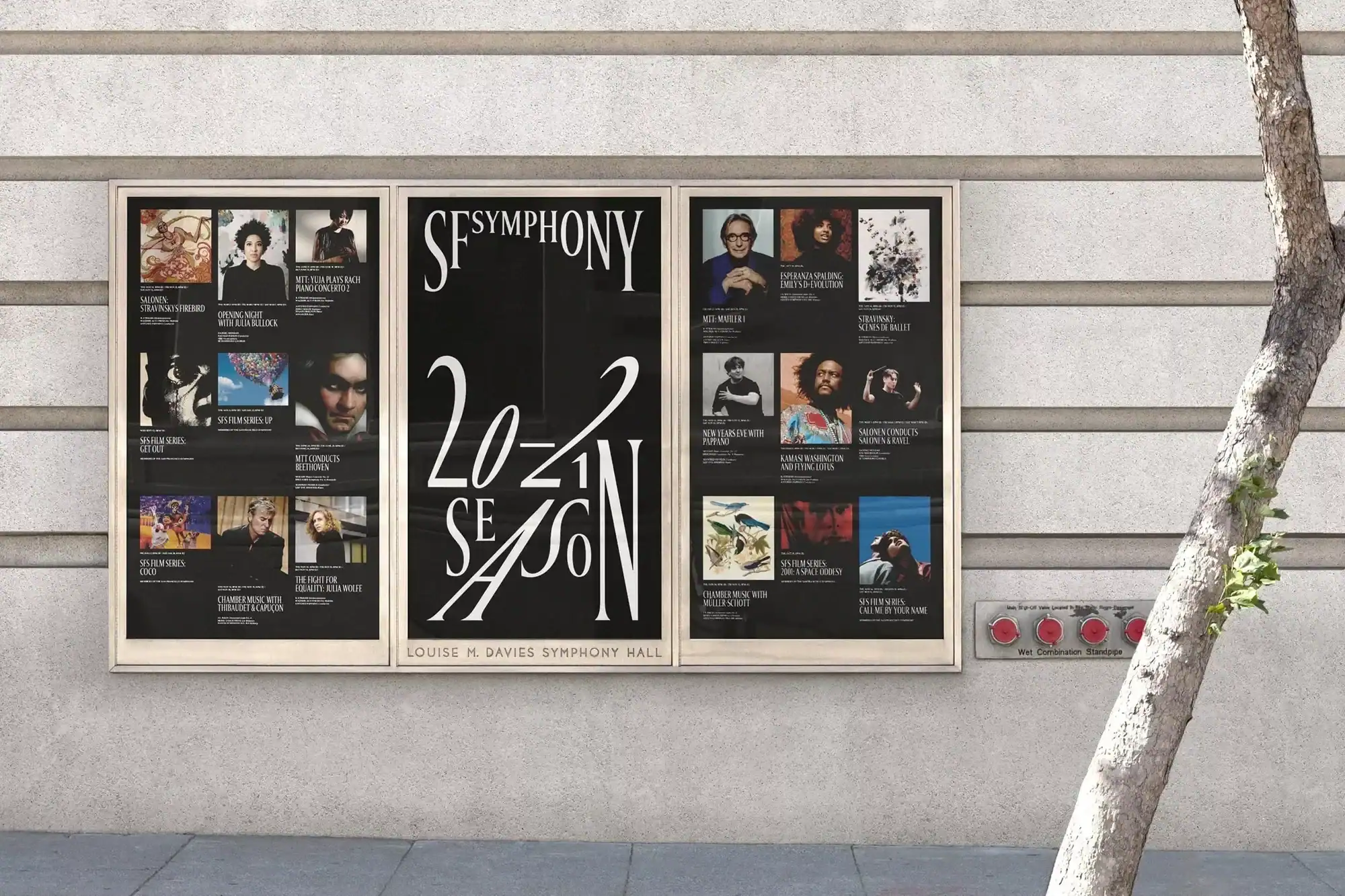 Three framed posters advertising a symphony season mounted on a light concrete wall, with a tree trunk nearby.