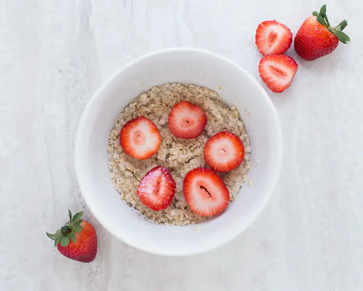 White bowl of oatmeal topped with strawberry slices on a light marble surface